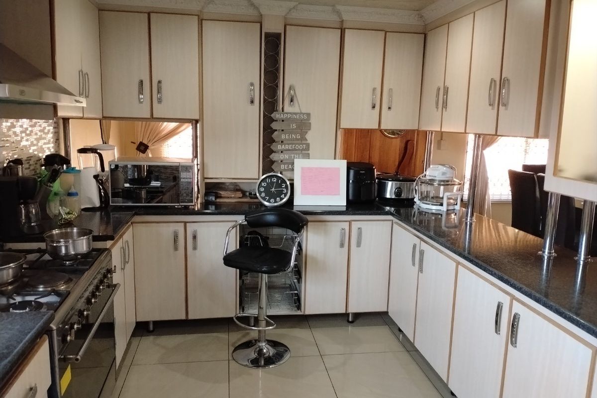 A functional kitchen featuring light-toned laminate cabinetry, dark granite countertops, a gas hob with extractor fan, and tiled flooring.
