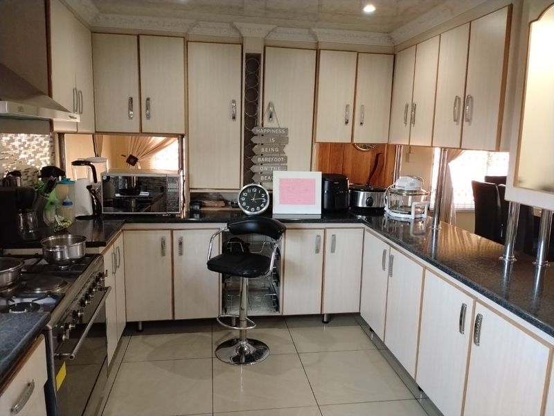 A functional kitchen featuring light-toned laminate cabinetry, dark granite countertops, a gas hob with extractor fan, and tiled flooring.