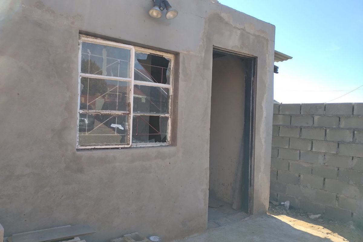 Exterior view of a structure featuring unfinished cement plaster walls, a broken window, and an open doorway, requiring significant maintenance and repair.