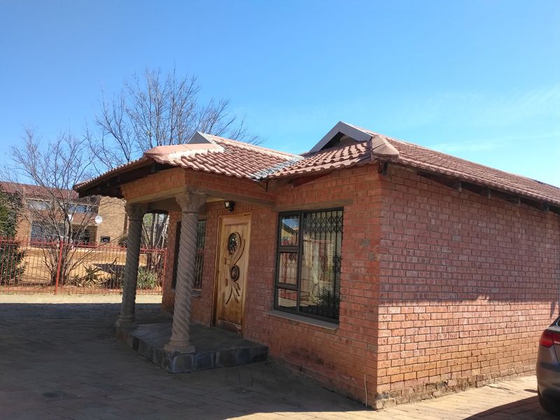 Front view of a face brick house featuring a covered porch with decorative columns, tiled roof, and paved driveway access.