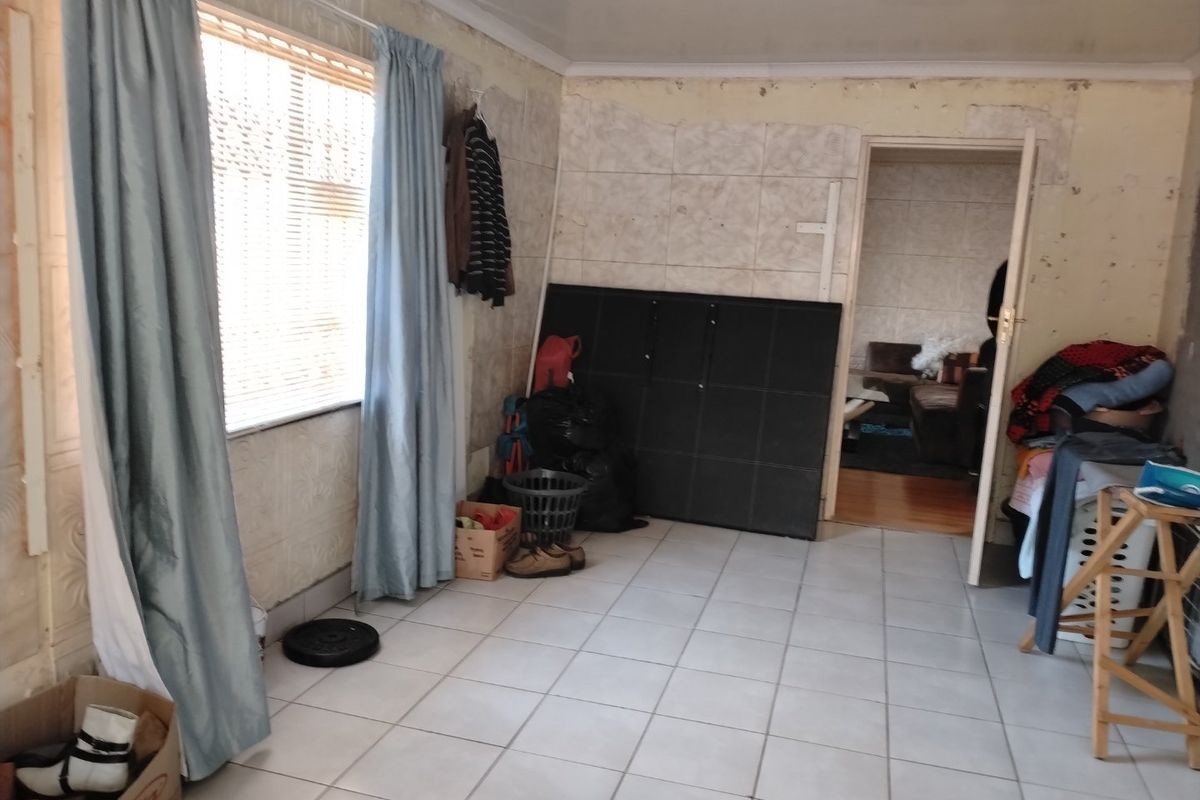 A living area featuring tiled flooring and a window with blinds, currently requiring significant cosmetic updates to the wall finishes.