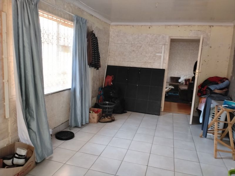 A living area featuring tiled flooring and a window with blinds, currently requiring significant cosmetic updates to the wall finishes.