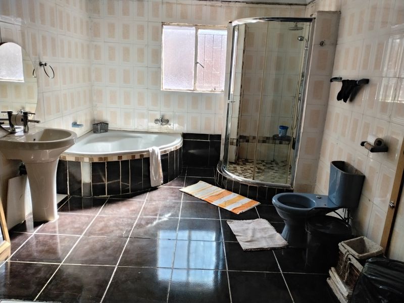 A dated bathroom featuring a corner bathtub, separate shower enclosure, pedestal basin, and toilet with dark floor tiles and light wall tiling.