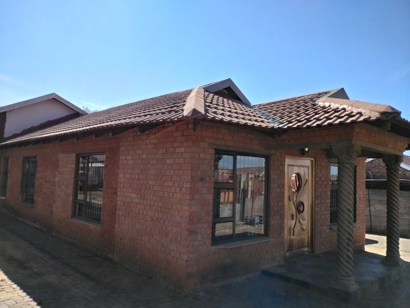 A well-maintained face brick house featuring a tiled roof, decorative stone columns at the entrance, and a paved driveway.