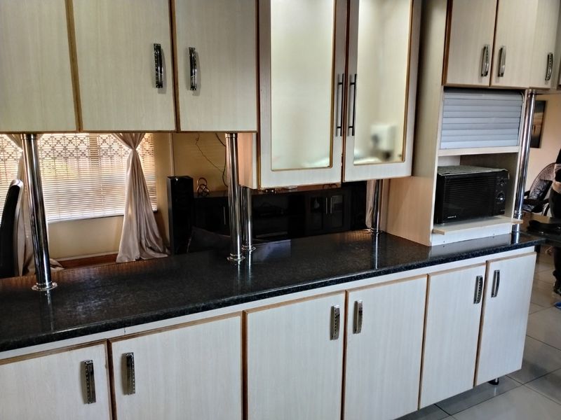 A functional kitchen area featuring light-toned laminate cabinetry, dark granite countertops, and integrated microwave space with glass-fronted display cabinets.