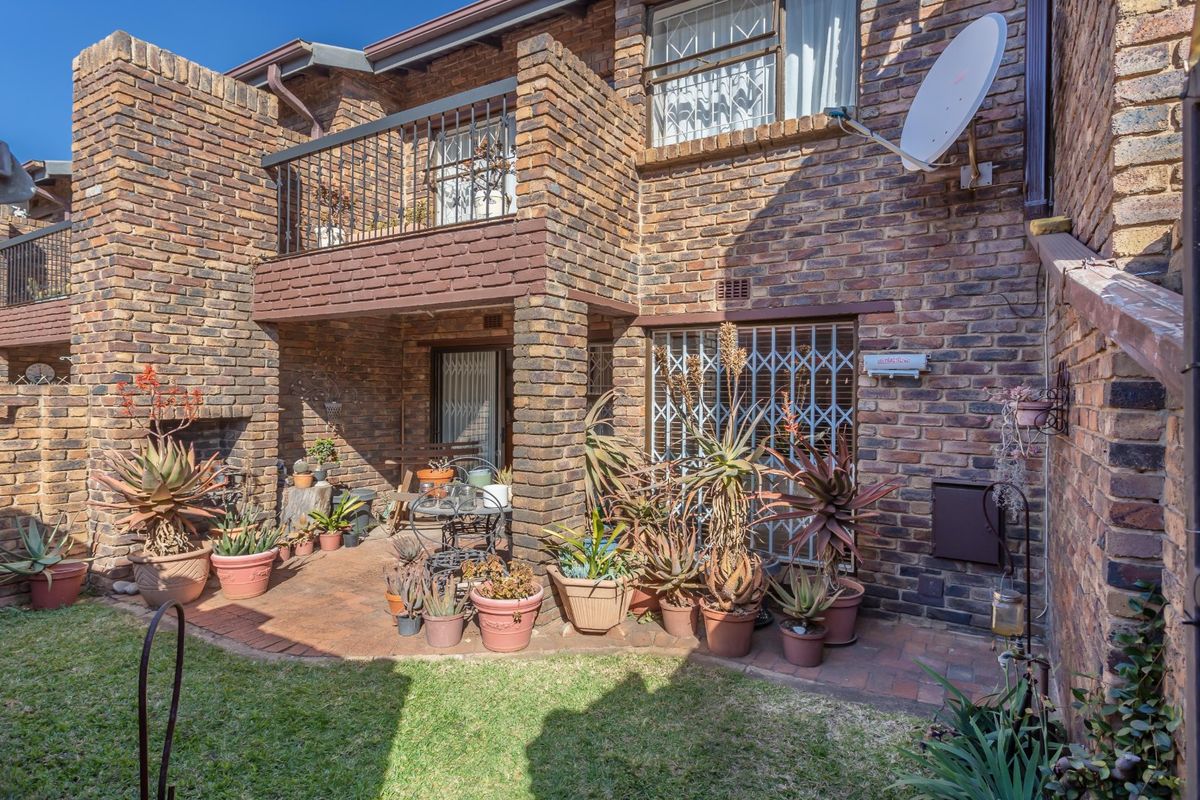 Rear view of a face brick townhouse featuring a paved patio, built-in outdoor fireplace, and an upper-level balcony with metal security railings.
