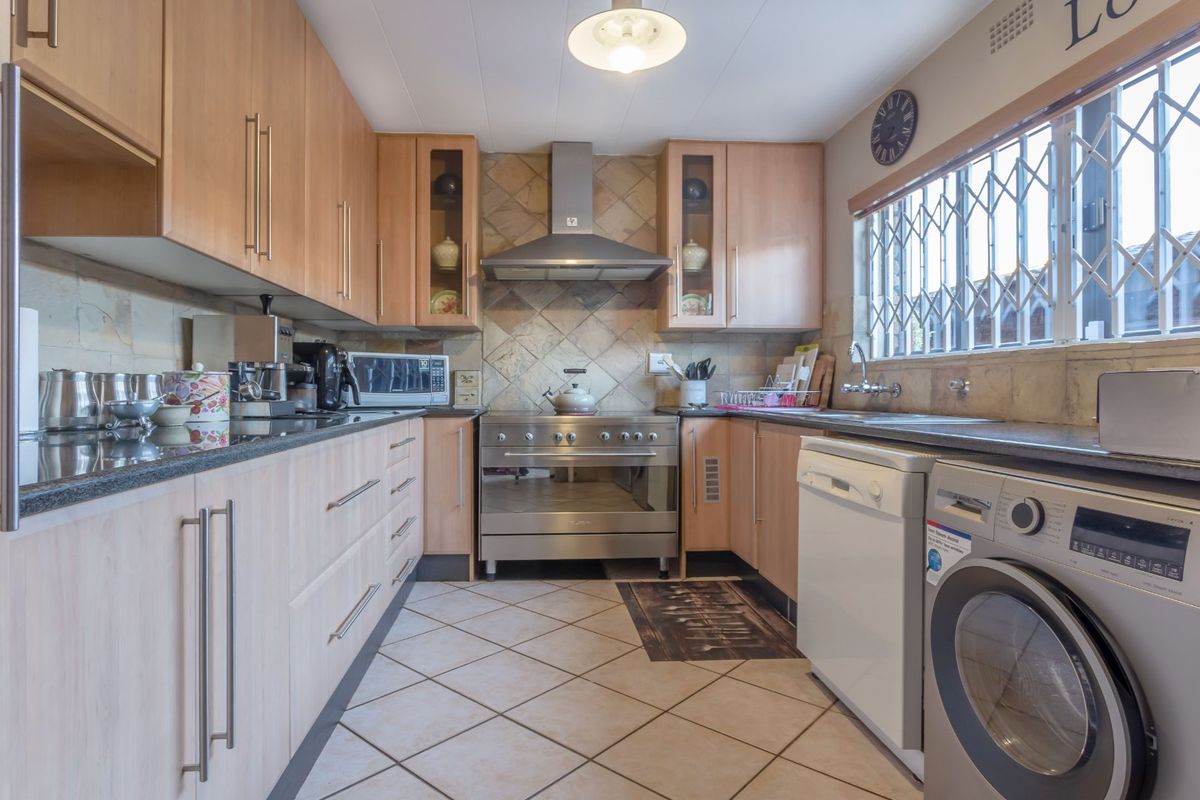 Functional kitchen featuring light wood cabinetry, granite countertops, stainless steel oven with extractor fan, and tiled finishes throughout.