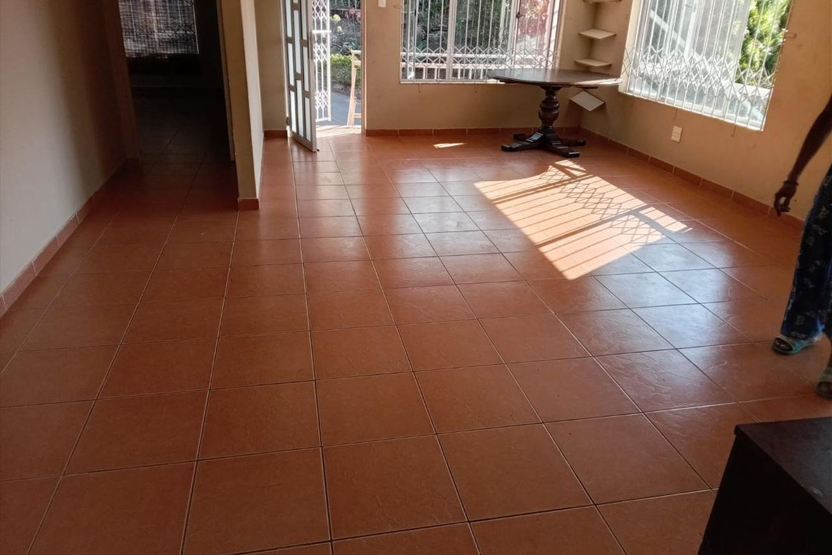 Spacious living area featuring terracotta-style ceramic floor tiles, large windows with security burglar bars, and a sliding door leading to the exterior.