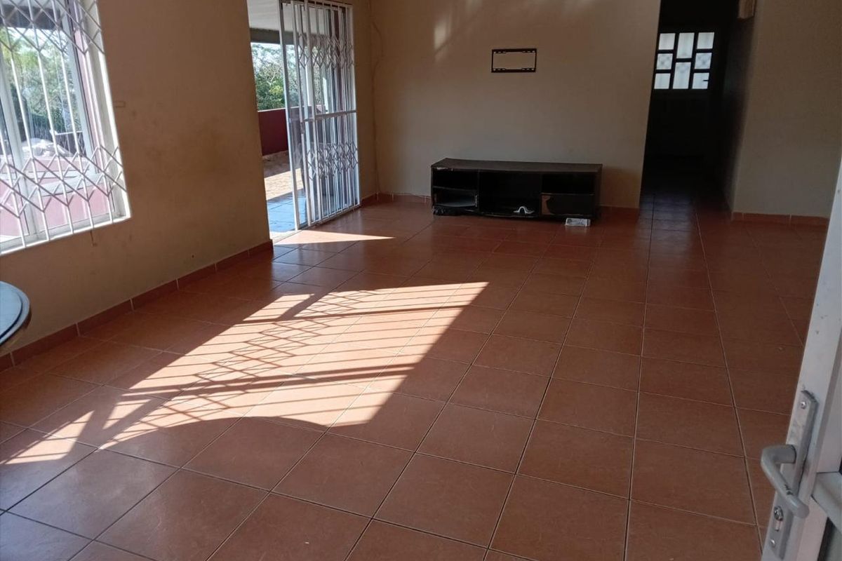 Spacious, empty living room featuring ceramic floor tiles, security gates, and access to an outdoor area, providing a blank canvas for renovation.