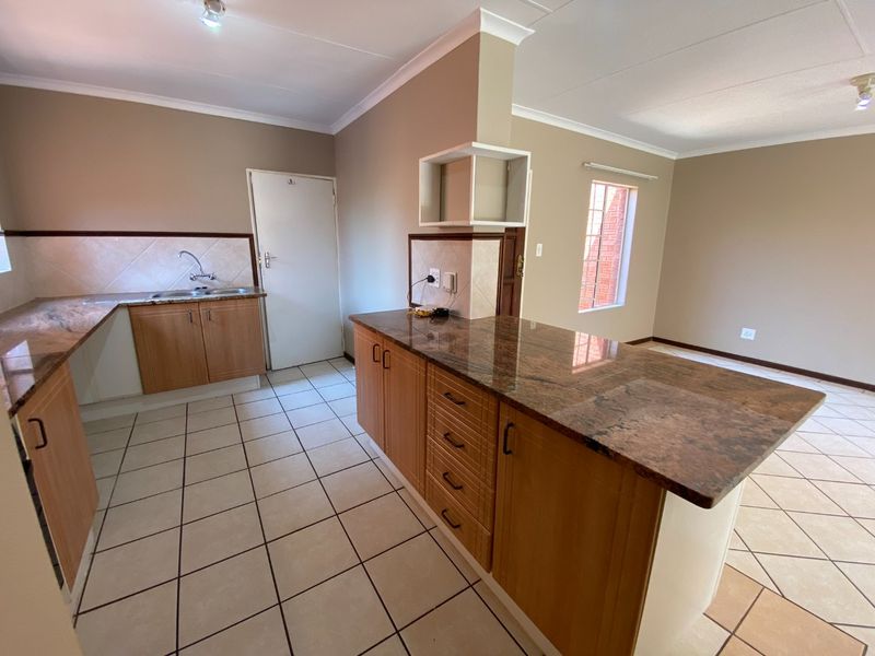 Open plan kitchen area featuring granite countertops, wooden cabinetry, and ceramic floor tiles, offering a functional and neutral space ready for personalization.