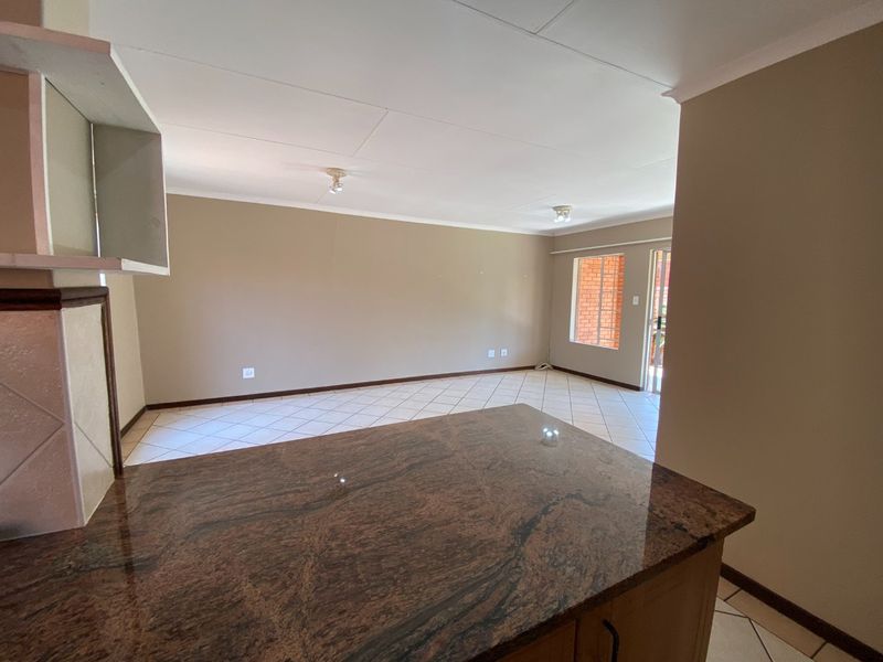 An open-plan living area featuring tiled flooring, a granite breakfast bar, and access to an outdoor space through a sliding door.