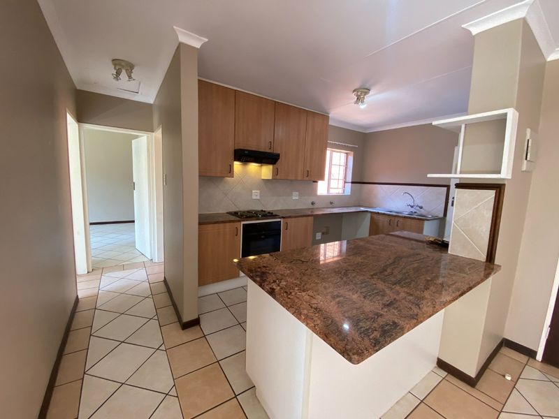 A functional kitchen featuring granite countertops, built-in oven, gas hob, and a breakfast nook, with tiled flooring and neutral cabinetry.