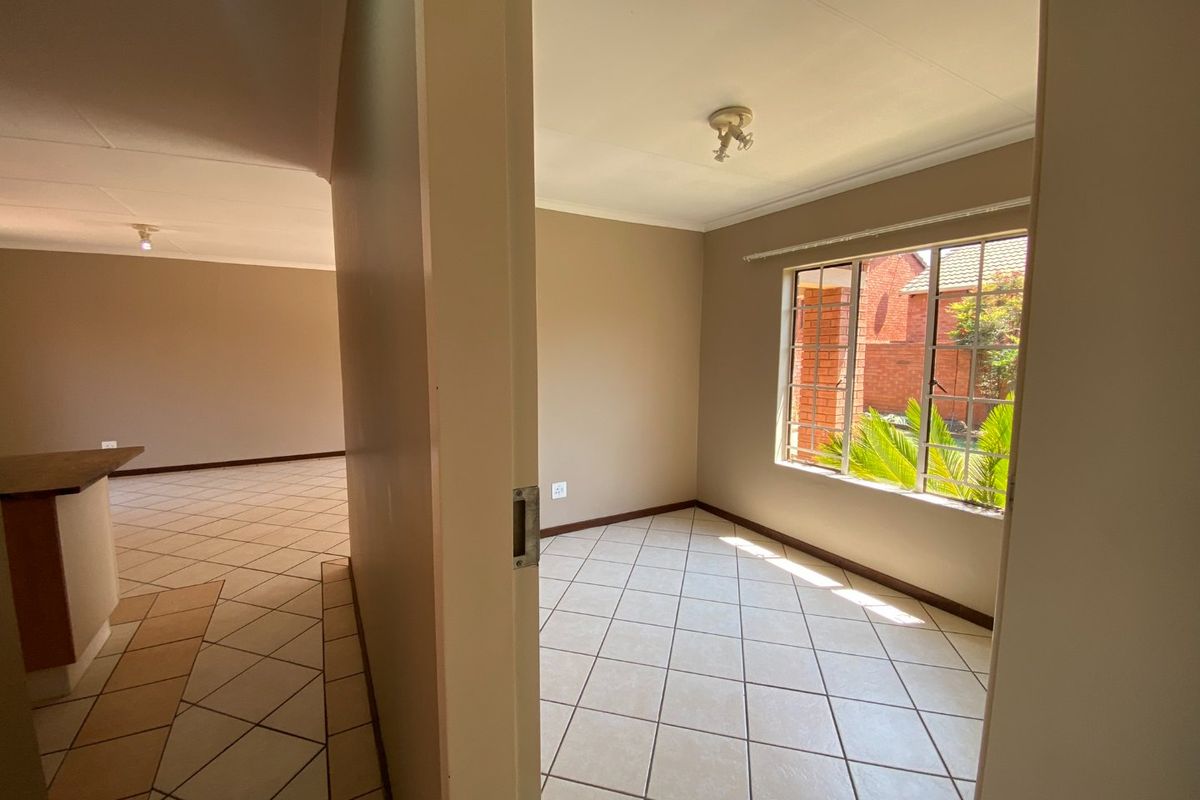 A bright, empty bedroom featuring neutral wall tones, tiled flooring, and a window with security bars, offering a clean canvas for personalization.