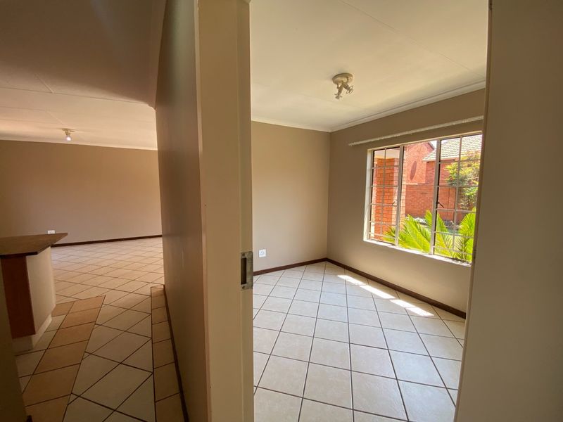 A bright, empty bedroom featuring neutral wall tones, tiled flooring, and a window with security bars, offering a clean canvas for personalization.