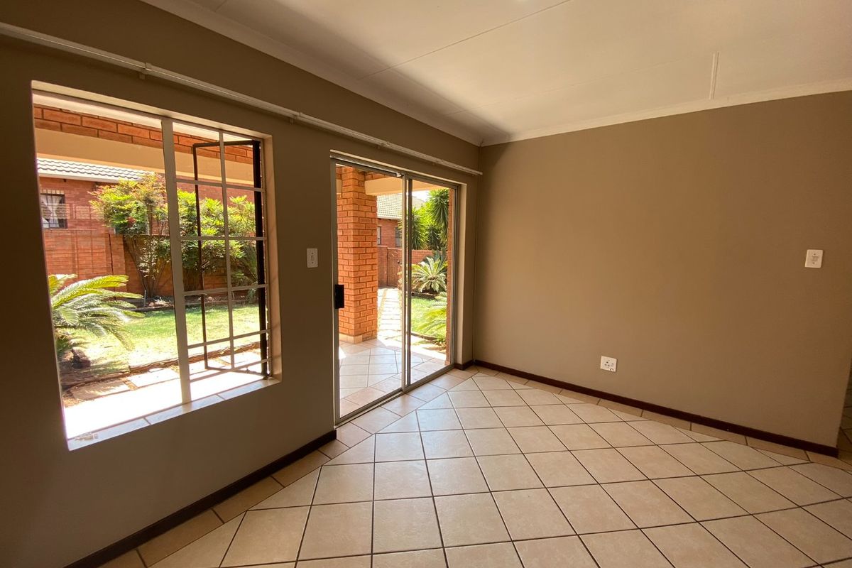 A bright, empty living room featuring tiled flooring, large windows, and a sliding glass door providing direct access to the outdoor patio and garden area.