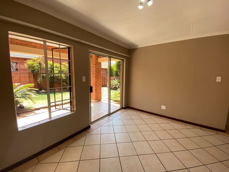 A bright, empty living room featuring tiled flooring, large windows, and a sliding glass door providing direct access to the outdoor patio and garden area.