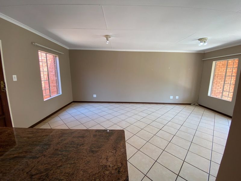 Spacious open-plan living area featuring neutral wall tones, ceramic tiled flooring, and natural light through windows with security bars.