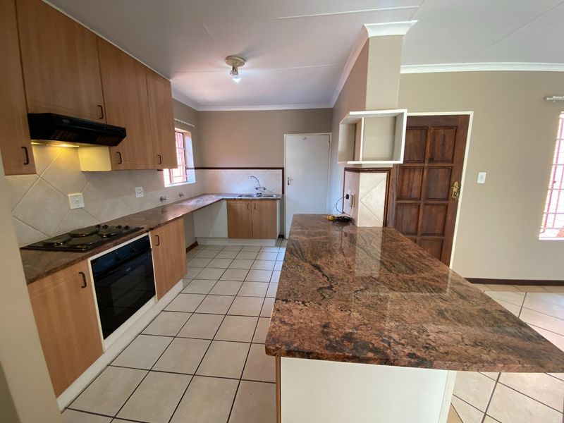 A functional kitchen featuring granite countertops, wooden cabinetry, built-in oven and hob, and a breakfast bar, with tiled flooring throughout.