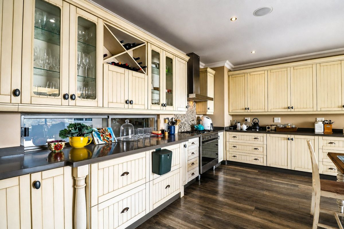 A well-maintained kitchen featuring cream-colored cabinetry, stone countertops, integrated stainless steel appliances, and warm laminate flooring with recessed lighting.