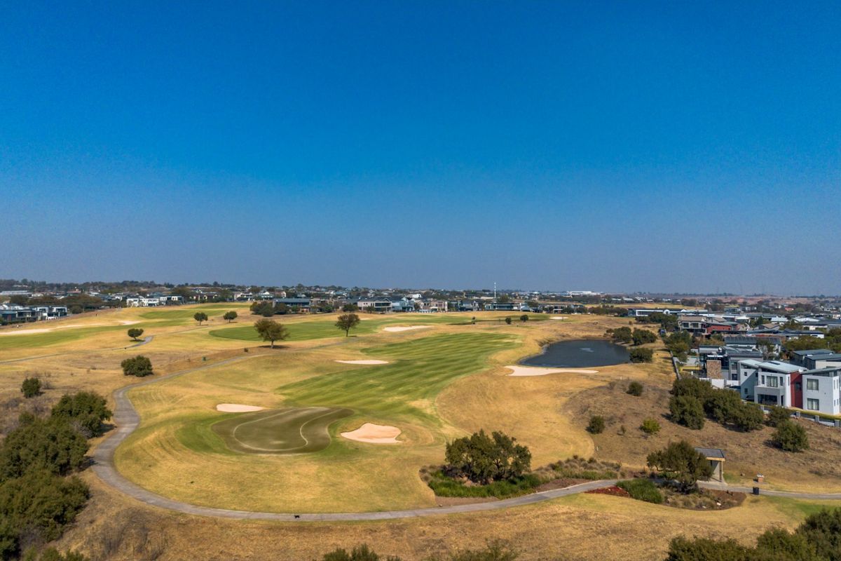 An aerial view of a residential golf estate featuring manicured fairways, sand bunkers, a water hazard, and surrounding modern housing developments.