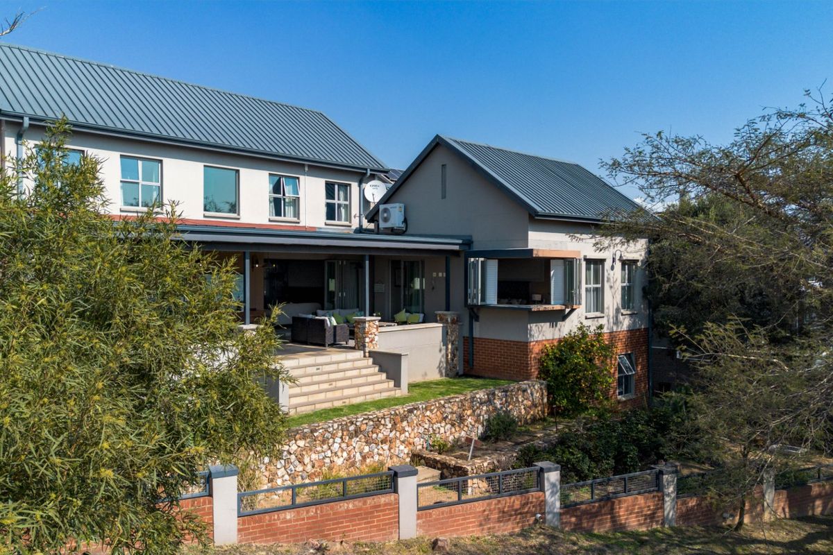 Rear view of a multi-story house featuring a covered patio, stone retaining wall, and brick boundary fencing.