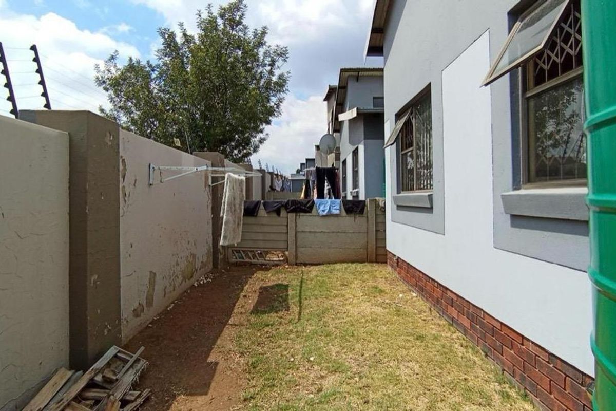 Side yard area featuring a perimeter wall with electric fencing, a water storage tank, and brick foundation detailing along the house exterior.