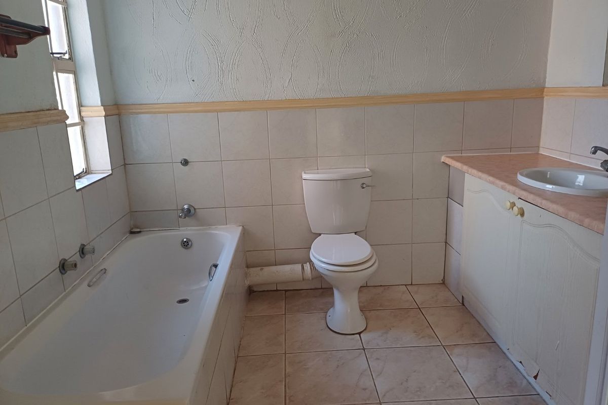 A dated bathroom featuring a standard bathtub, toilet, and vanity basin with tiled finishes, requiring cosmetic updates to improve its overall condition.