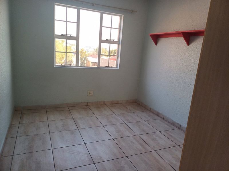 An empty bedroom featuring tiled flooring, a window with security bars, and a wall-mounted shelf.
