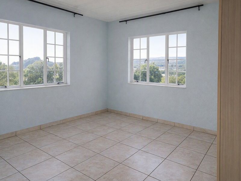 A bright, empty bedroom featuring neutral tiled flooring, built-in cupboard storage, and large windows offering natural light and scenic views.