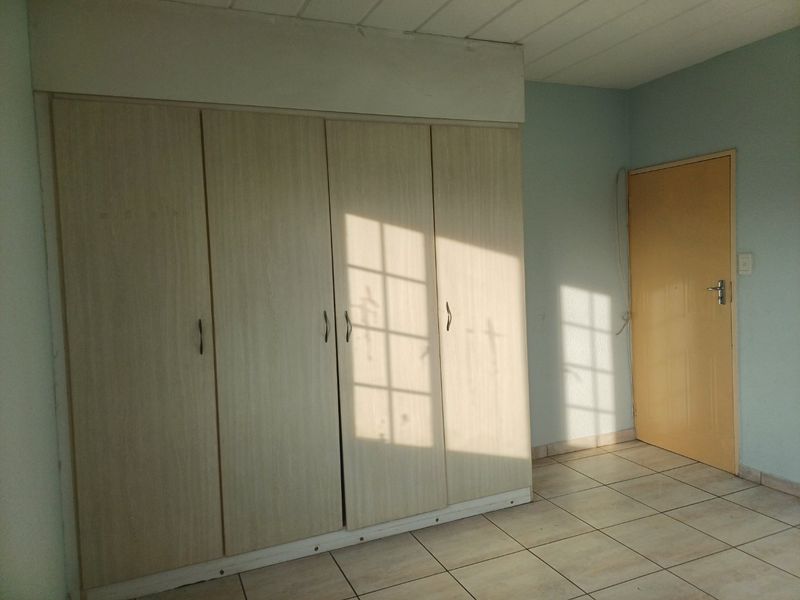 A bedroom featuring built-in cupboards, tiled flooring, and a neutral wall finish, offering a clean and functional space ready for personalization.