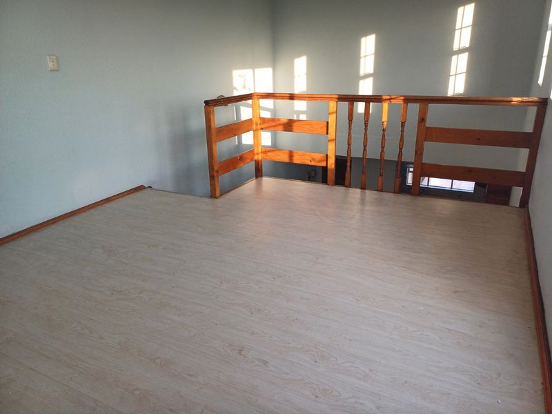 An empty mezzanine-style loft area featuring light-toned laminate flooring and a traditional wooden balustrade overlooking the lower level.