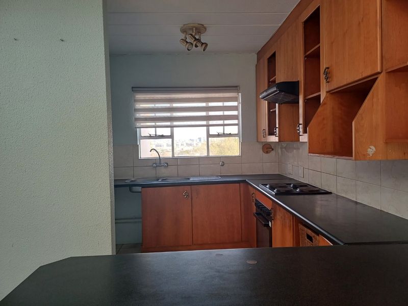 A functional kitchen featuring built-in wooden cabinetry, laminate countertops, a double sink, and integrated cooking appliances with a tiled backsplash.