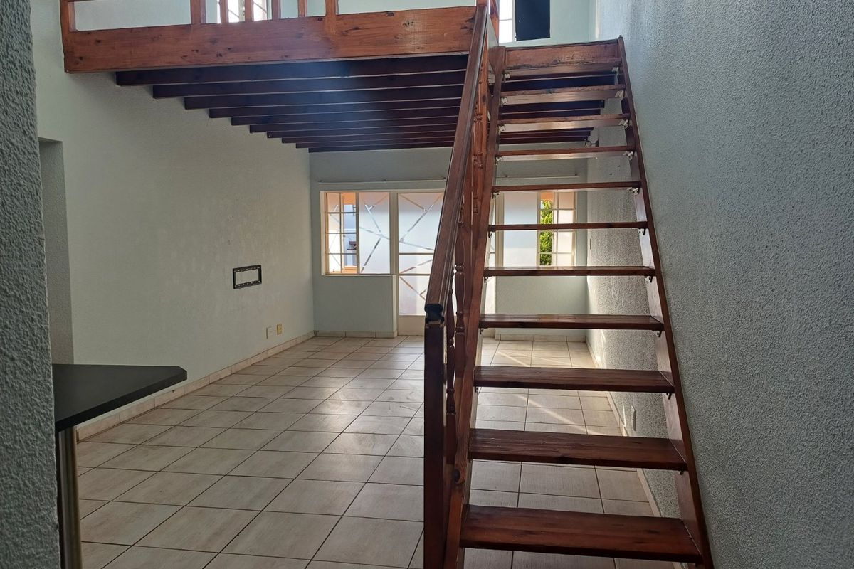 Open plan living area featuring a wooden staircase leading to a mezzanine level, tiled flooring, and a breakfast bar.