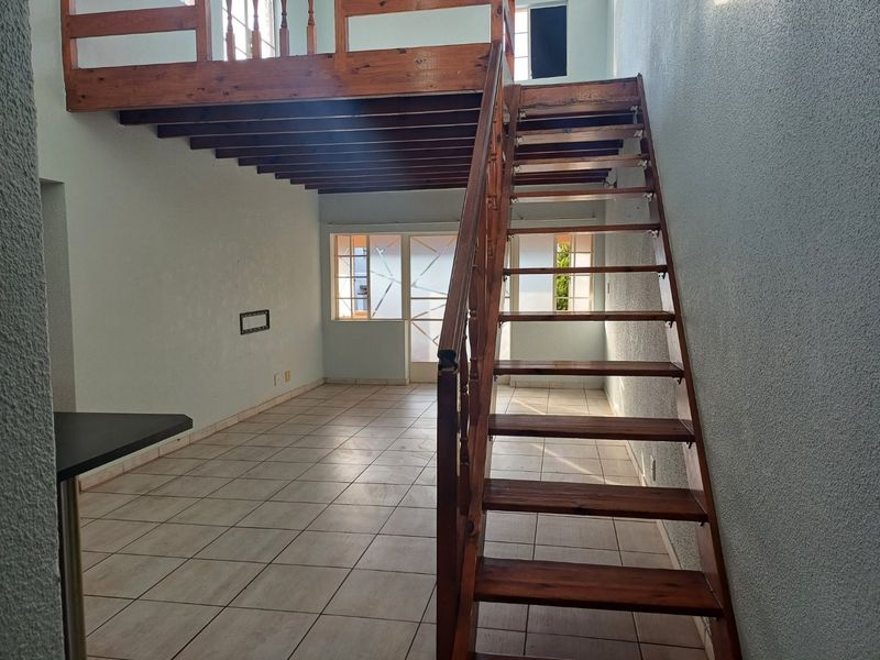 Open plan living area featuring a wooden staircase leading to a mezzanine level, tiled flooring, and a breakfast bar.