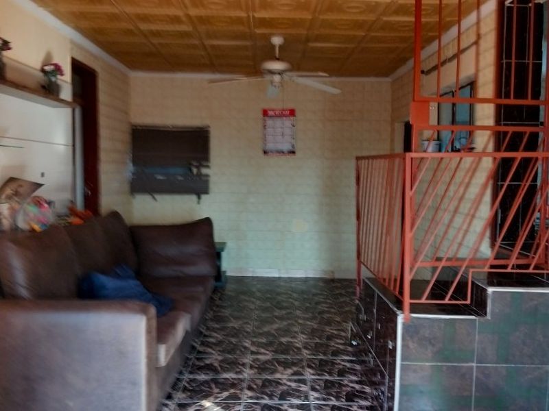 Living area featuring decorative ceiling tiles, a ceiling fan, and tiled flooring with an integrated staircase and metal security gate.