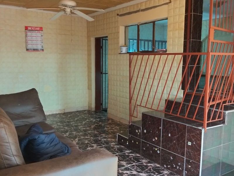 Living area featuring decorative ceiling tiles, tiled flooring, and a metal staircase railing, offering a dated aesthetic with potential for modernization.
