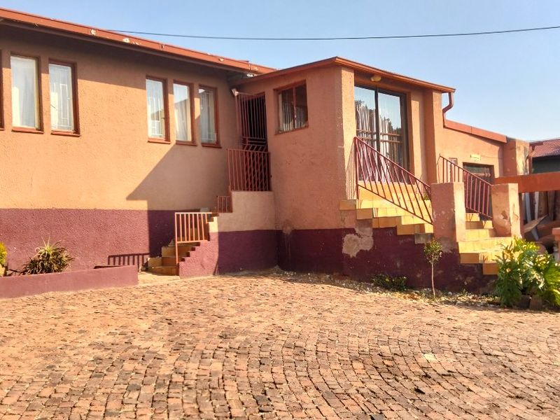 Front exterior view of a house featuring a cobblestone driveway, concrete stairs with metal railings, and a sliding glass door entrance.