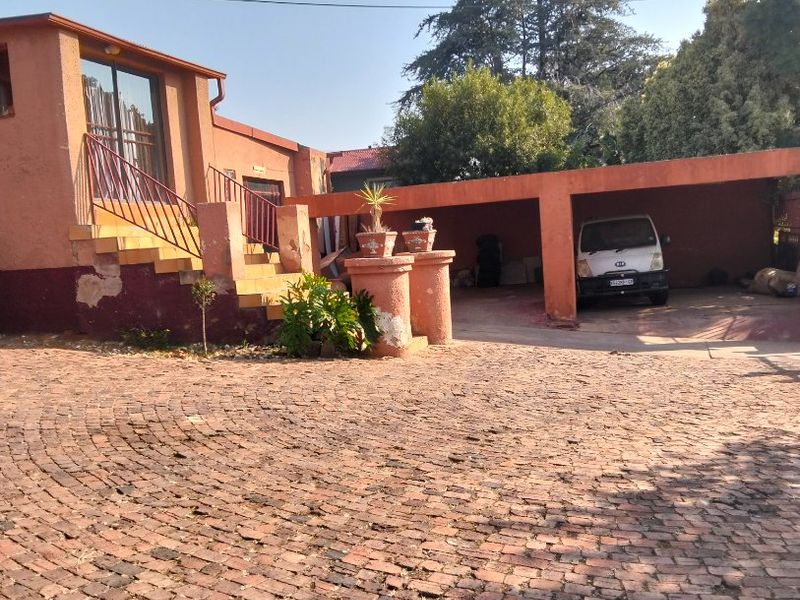 Front exterior view of the house featuring a brick paved driveway, a covered carport, and an elevated entrance with a staircase.