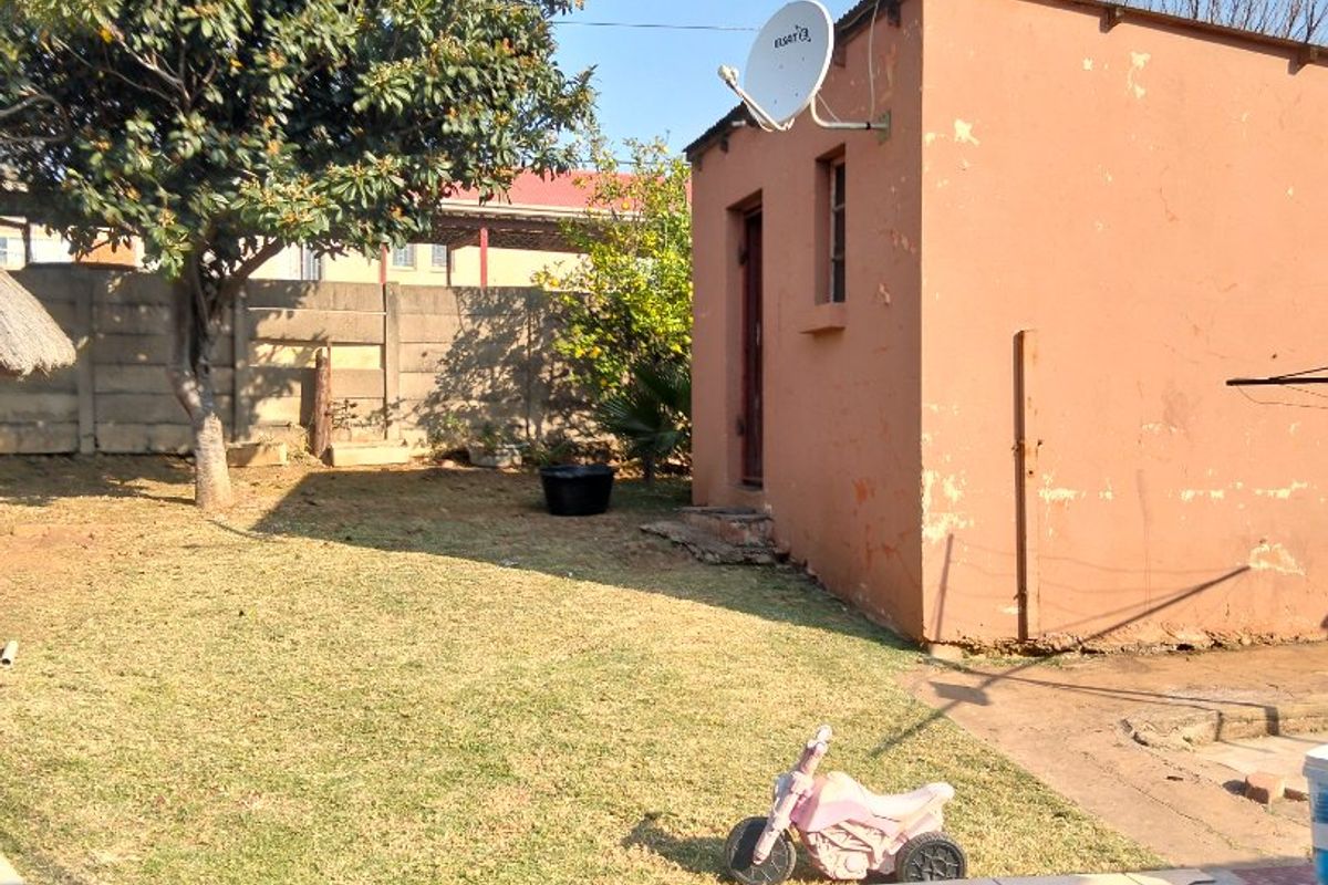 Rear garden area featuring a small masonry outbuilding, satellite dish, and a tiled patio with visible wear to the exterior finishes.