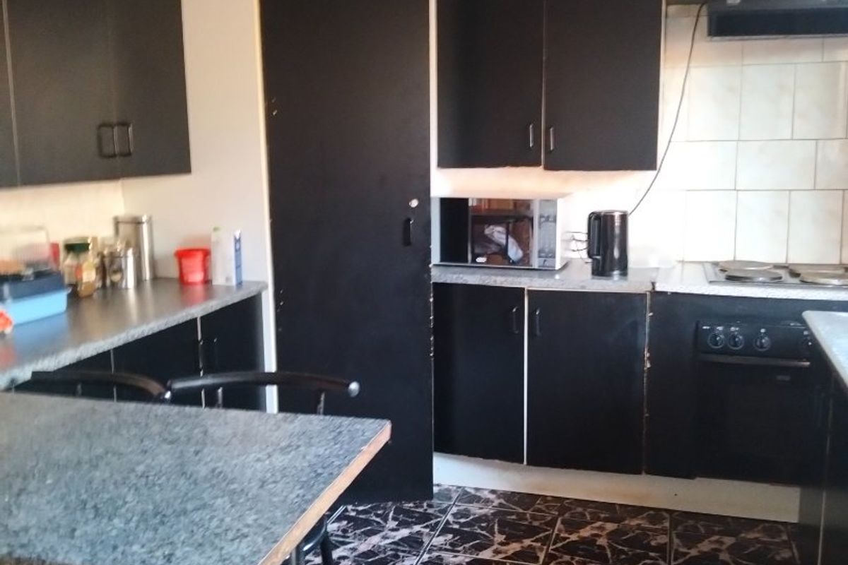 A functional kitchen featuring dark cabinetry, laminate countertops, built-in oven, hob, and extractor fan with a tiled backsplash and floor.