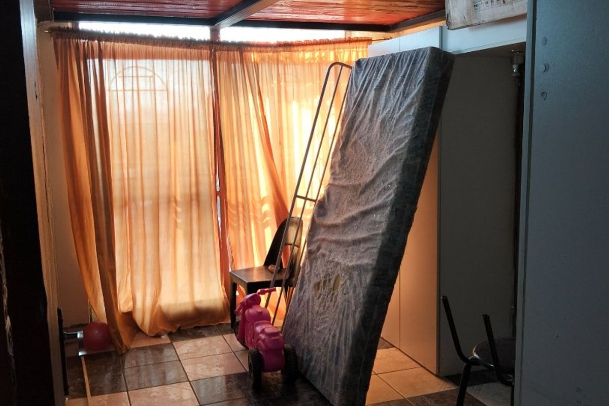 A bedroom space featuring exposed timber ceiling beams and tiled flooring, currently used for storage.