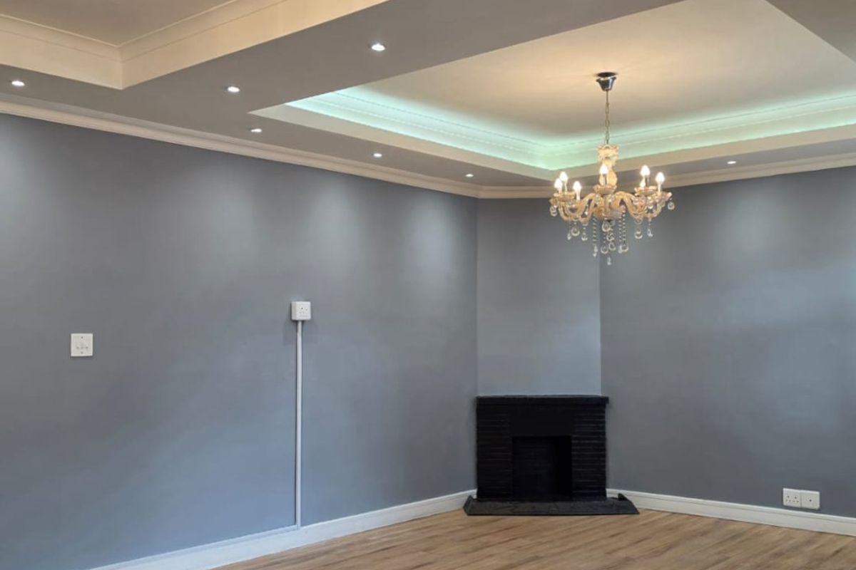 Spacious living room featuring a recessed ceiling with cove lighting, crystal chandeliers, corner fireplace, and modern laminate flooring.