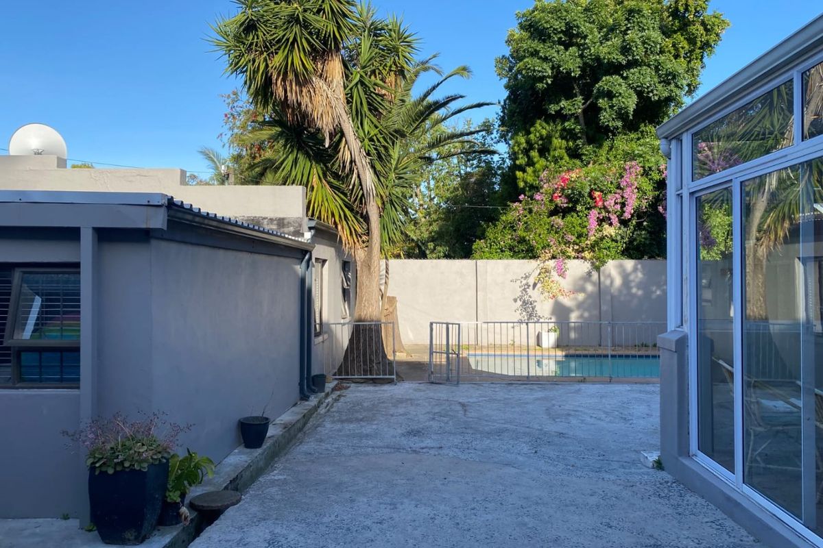Rear exterior view featuring a concrete patio area, swimming pool with safety fencing, and established garden boundary walls.