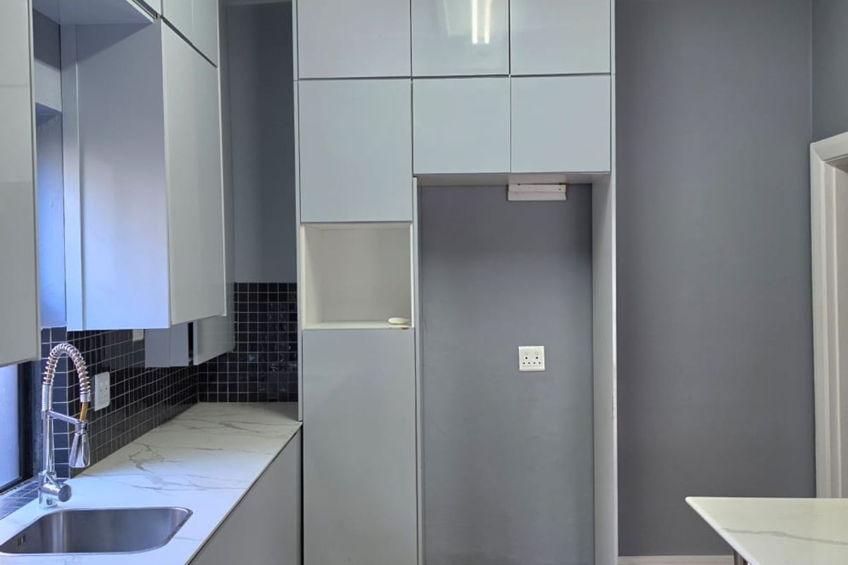 Modern kitchen featuring sleek grey cabinetry, marble-look countertops, mosaic tile backsplash, and dedicated refrigerator space with wood-look laminate flooring.