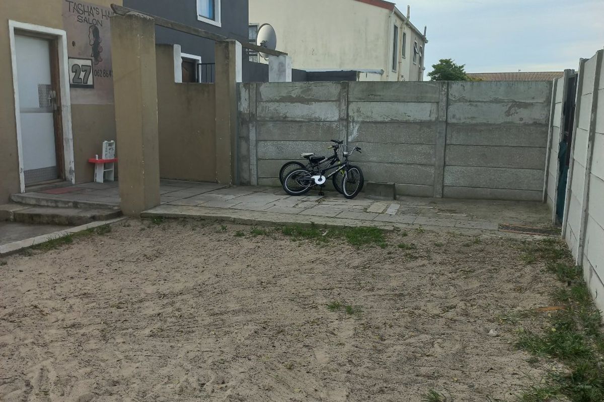 Rear exterior area featuring a paved patio section, concrete boundary walls, and an unlandscaped sandy yard space.
