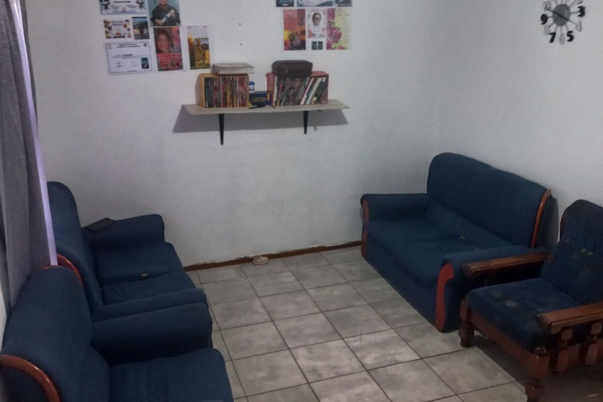 A modest living room featuring ceramic floor tiles and a wall-mounted shelf, providing a functional space for relaxation.