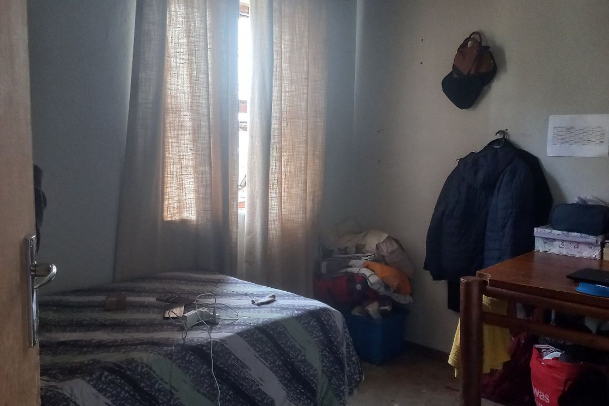 A compact bedroom featuring a window with curtains and basic finishes, requiring cosmetic updates to improve its overall appeal.