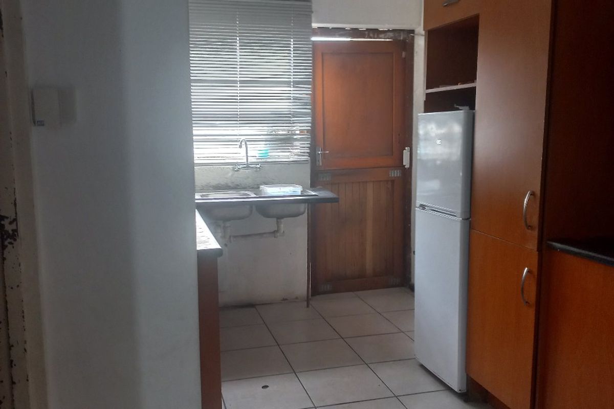 A functional kitchen area featuring tiled flooring, built-in wooden cabinetry, and a double sink with exposed plumbing.
