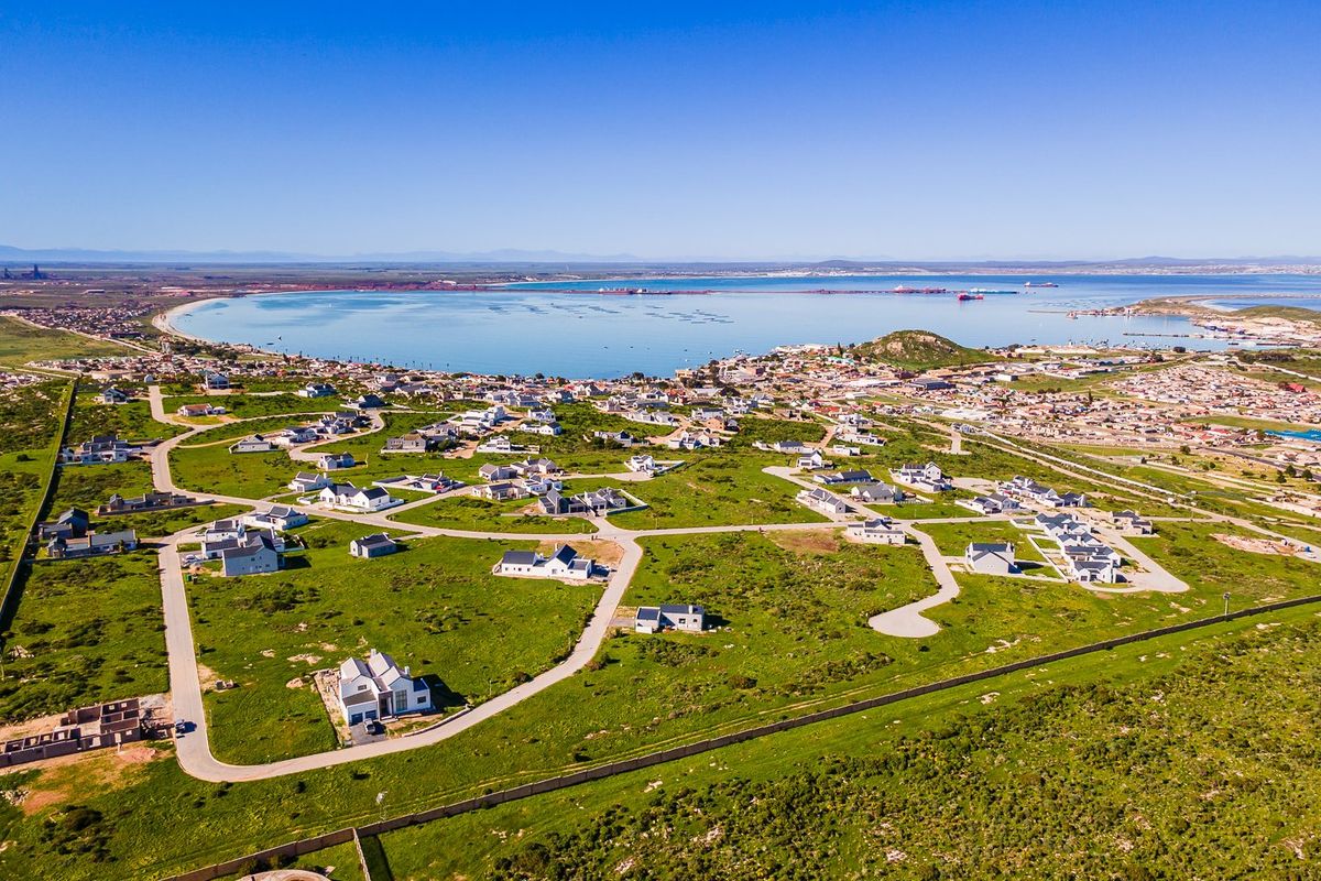 An aerial view of a residential estate development situated near the coastline, featuring paved roads and established housing plots.
