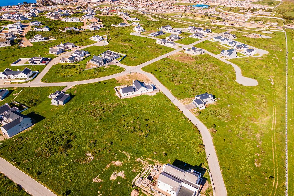 An aerial view of a residential development featuring vacant plots and established homes near the coastline.